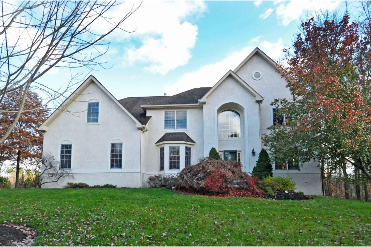 Westrum Corporate Two-story white house in Estates of Whitemarsh Hills with large windows, steep roof, and manicured lawn framed by autumn trees.
