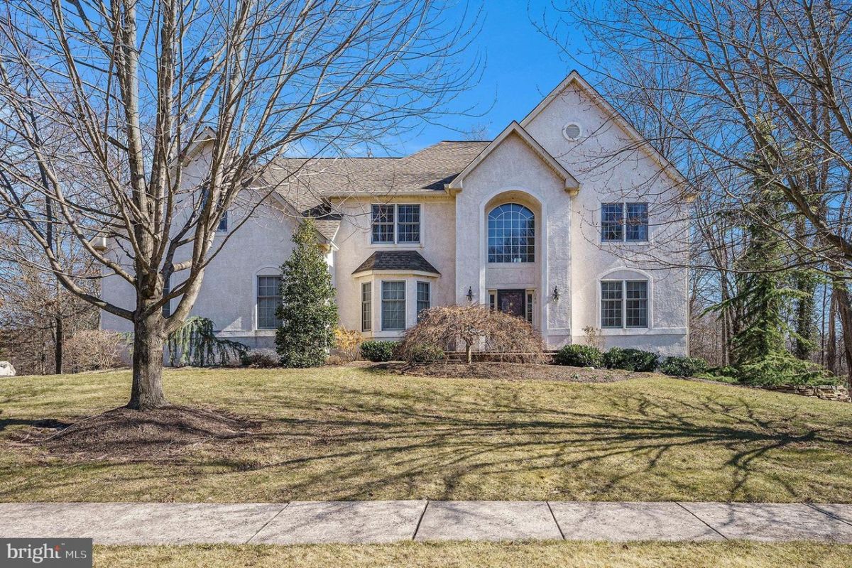 Westrum Corporate Charming two-story beige home in Kingswood Estates, featuring large windows and a landscaped yard with bare trees on a sunny day.