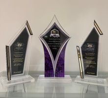 Westrum Corporate Three glass and acrylic awards on a white shelf, featuring gold accents and engraved plaques with text.