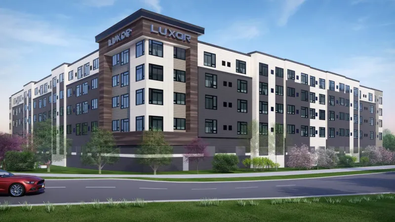 Westrum Corporate Modern five-story Luxor apartment in Fort Washington, featuring large windows, greenery, and a red car driving by out front.