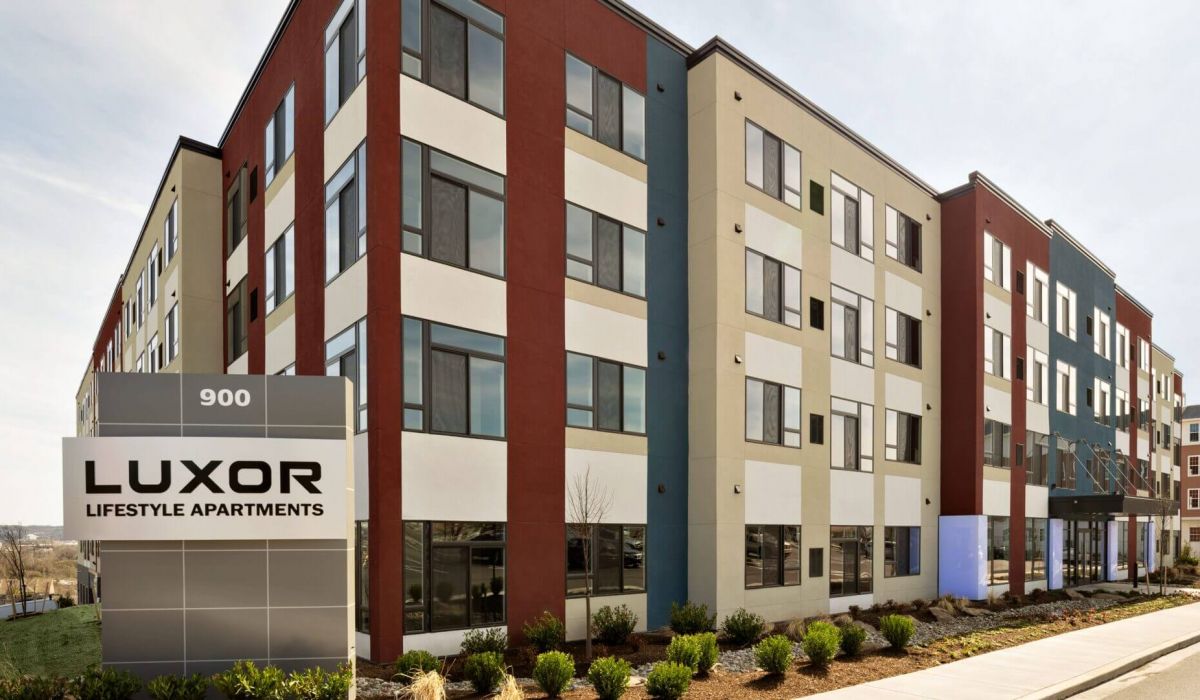 Westrum Corporate Modern four-story building with red, beige, and white accents; Luxor Lifestyle Apartments sign stands prominently in front.