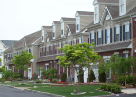 Westrum Corporate Row of modern townhouses with brick facades, dormer windows, and green trees lining the landscaped front yards.