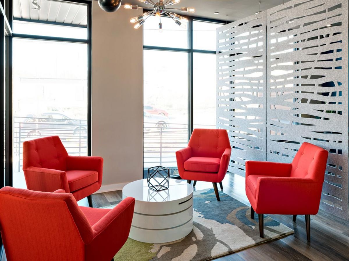 Westrum Corporate Four bright red armchairs surround a white table in The Pointe at 31′s modern Brewerytown lounge with large windows and a room divider.