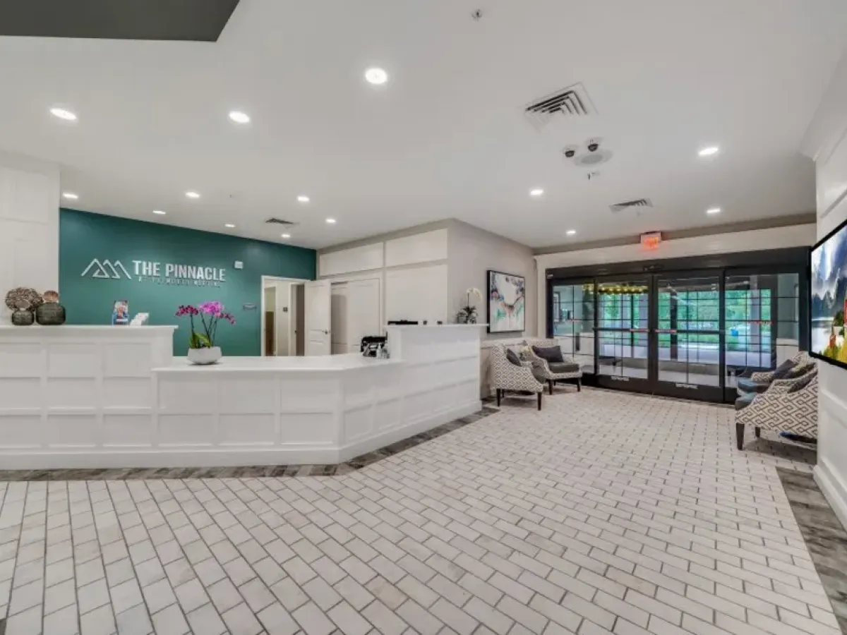 Westrum Corporate Modern lobby at Pinnacle at Plymouth Meeting features a white reception desk, chic chairs, art, orchids, and glass doors to luxury apartments.
