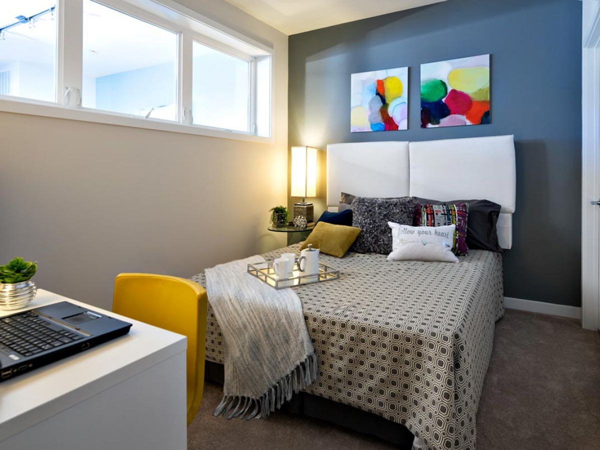 Westrum Corporate Small bedroom in 1200 Washington features a cozy bed, abstract art, and a desk with a plant—modern living in luxury apartments.