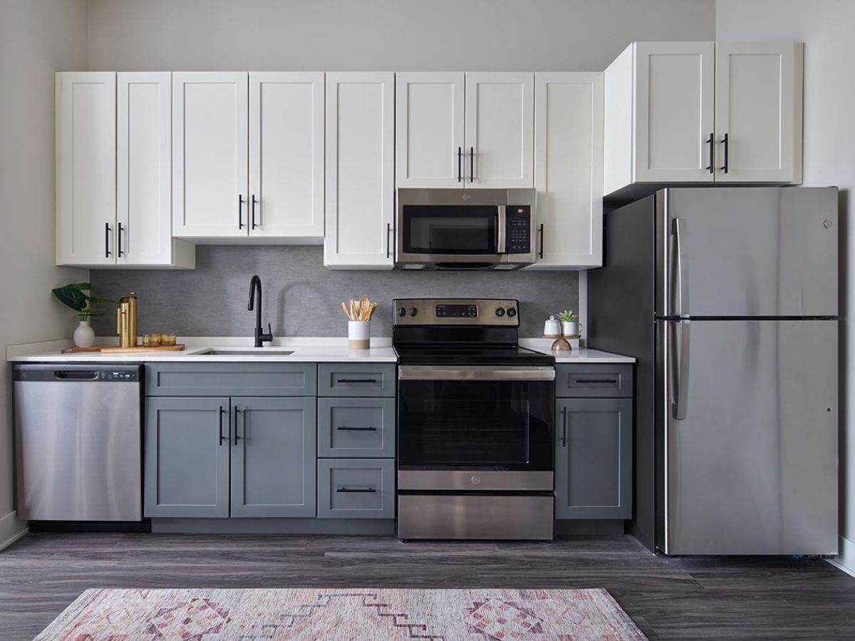 Westrum Corporate Modern kitchen in Luxor Wilmington features white and gray cabinets, stainless appliances, and a patterned rug on dark wood flooring.