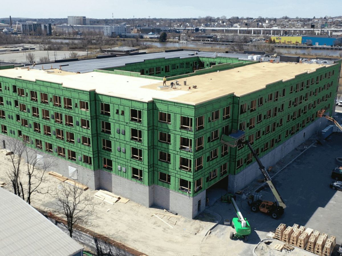 Westrum Corporate A large, green-insulated building under construction with cranes and workers around the site on a clear day.