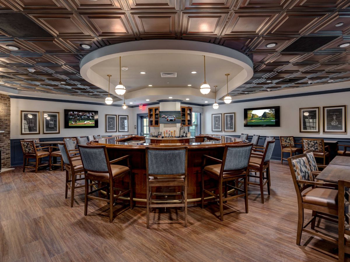 Westrum Corporate A modern bar with wooden floors, a round central counter, high chairs, TVs, wall art, and patterned ceiling tiles.