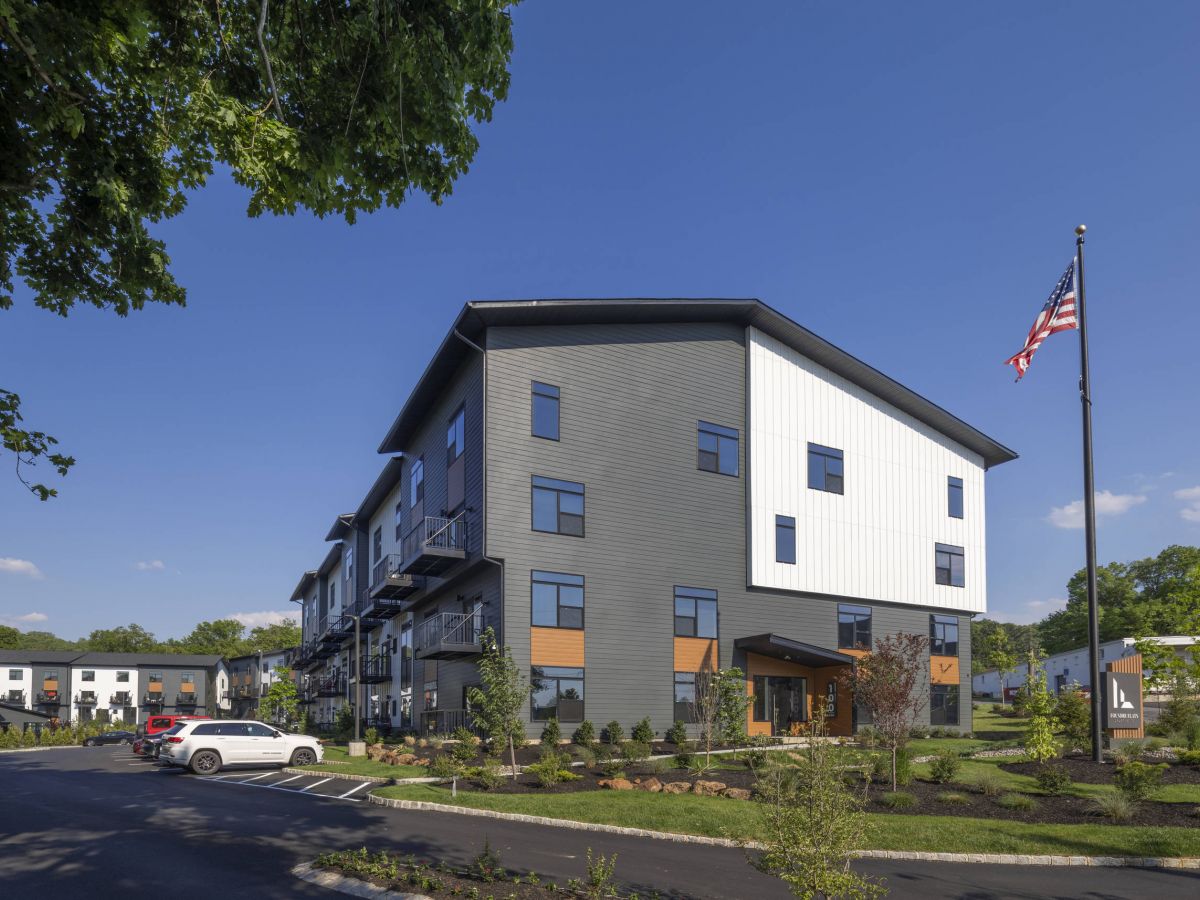 Westrum Corporate Foundry Flats is a modern three-story apartment building with cars parked outside, landscaped grounds, and an American flag on a sunny day.