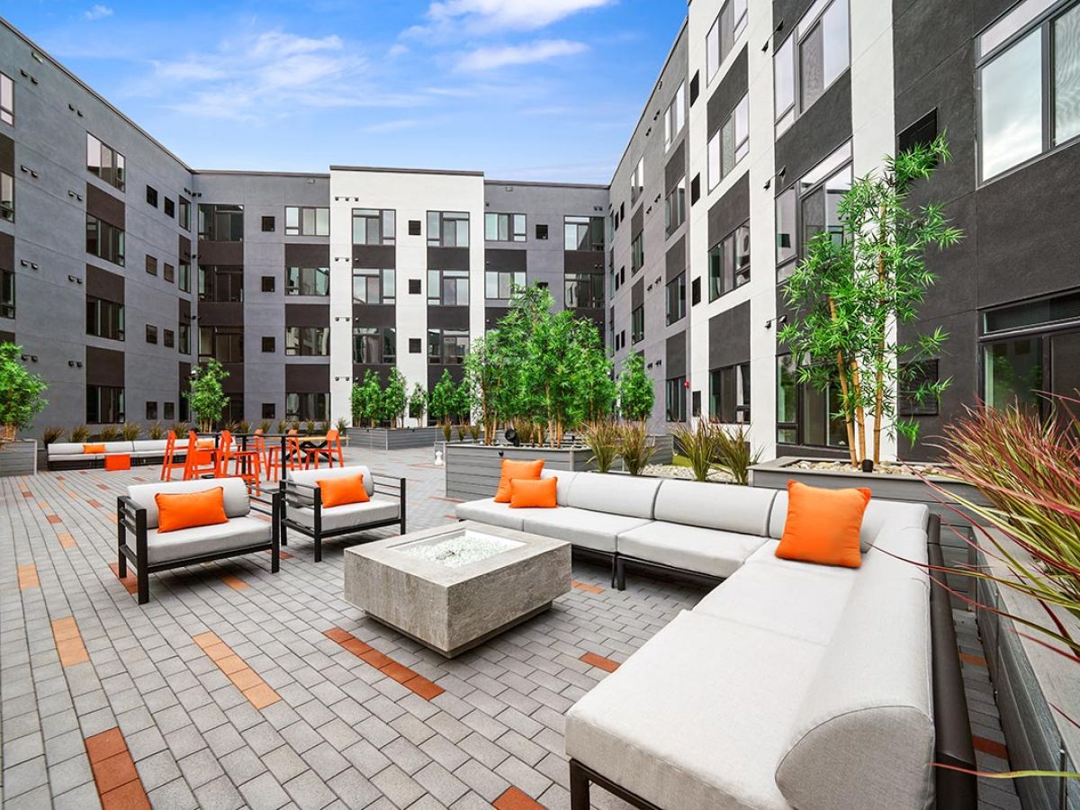 Westrum Corporate Modern Lansdale apartment courtyard with gray patio furniture, orange cushions, fire pit, and Luxor outdoor dining tables.