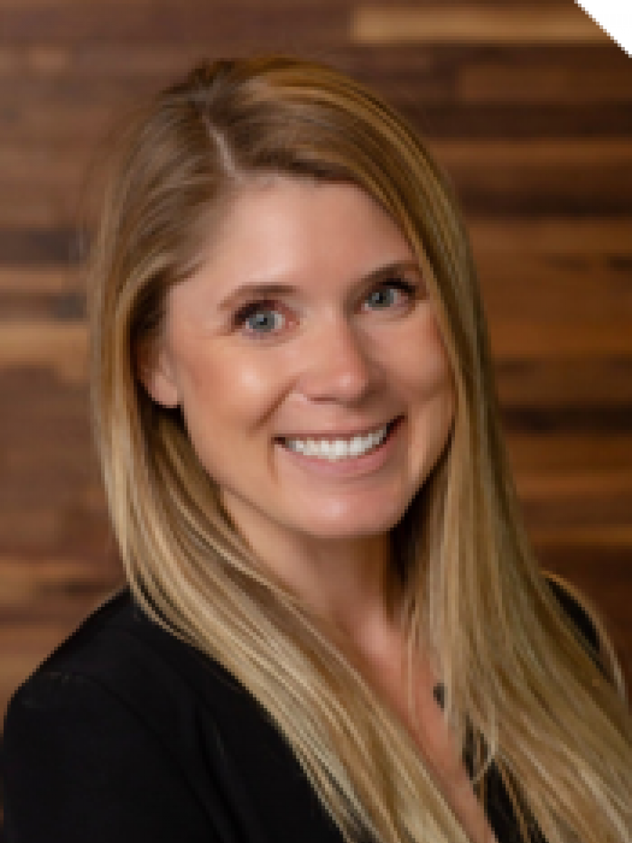 Westrum Corporate Smiling woman with long blonde hair wearing a black top, standing in front of a wooden background at the John Westrum event.