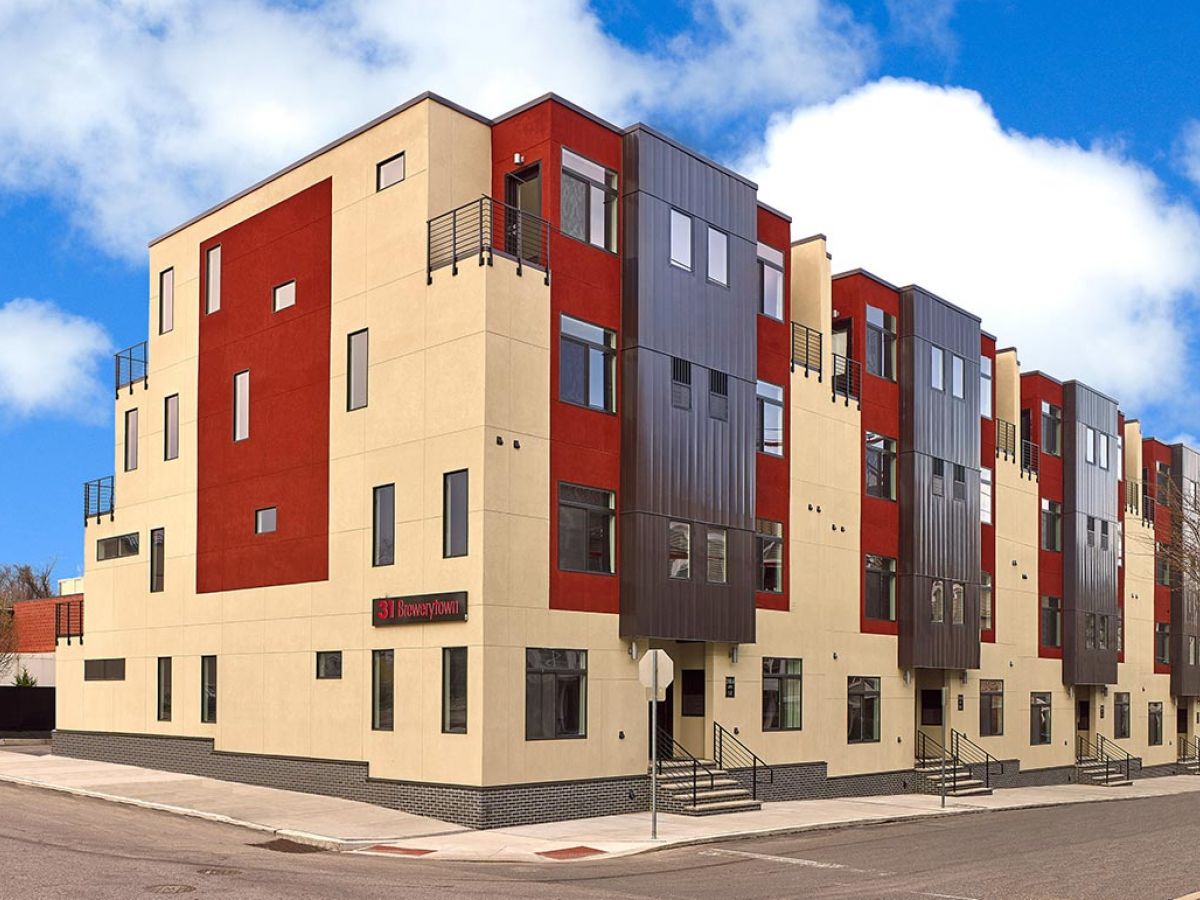 Westrum Corporate Modern, multi-story Flats at 31 Brewerytown feature red and beige exteriors on a lively city street corner under a blue sky.