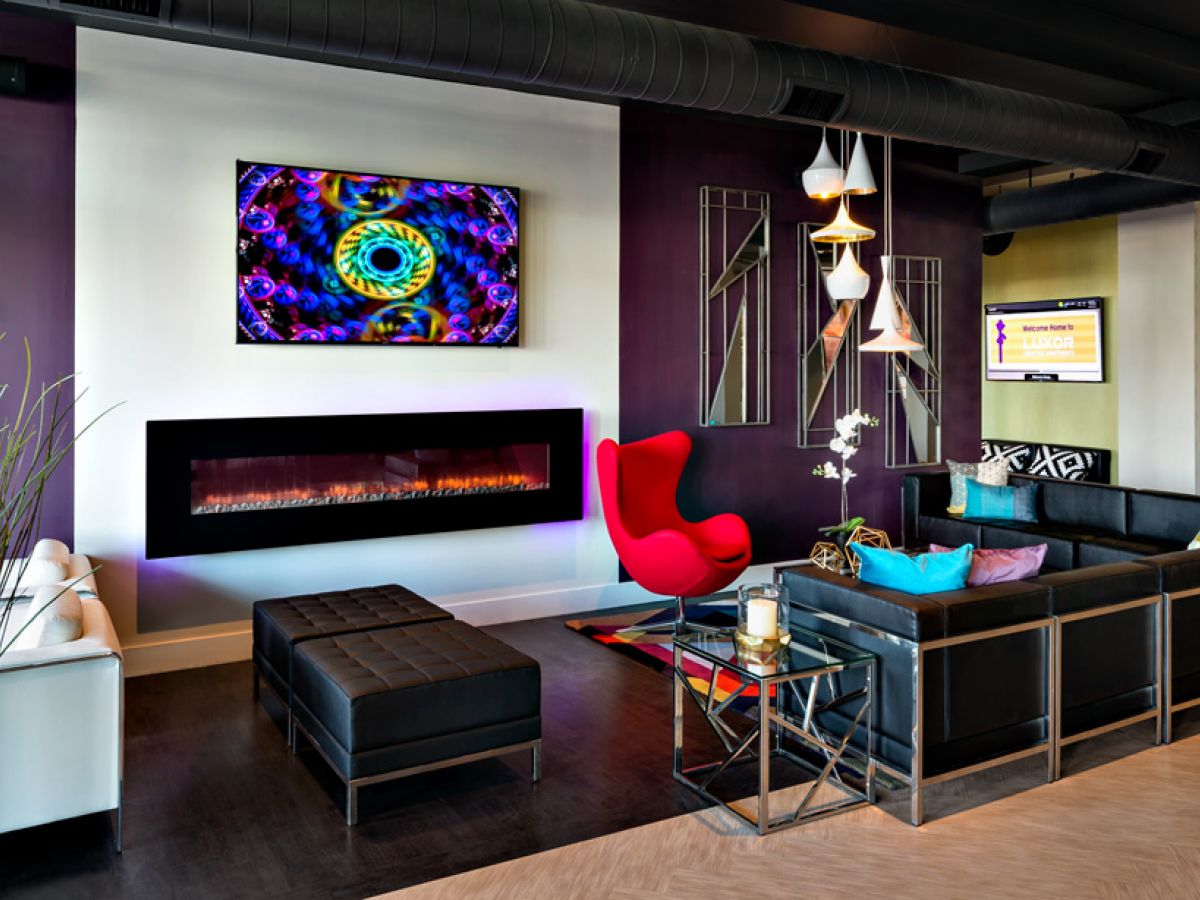 Westrum Corporate Modern lounge at Luxor Norristown with black sofas, red chair, wall fireplace, colorful art, and decorative plants.