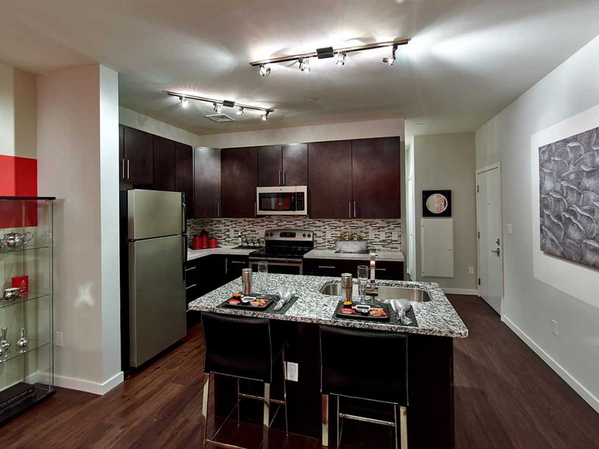 Westrum Corporate Modern kitchen in Flats at 31 Brewerytown, featuring dark cabinets, stainless steel appliances, and a stylish island with two place settings.