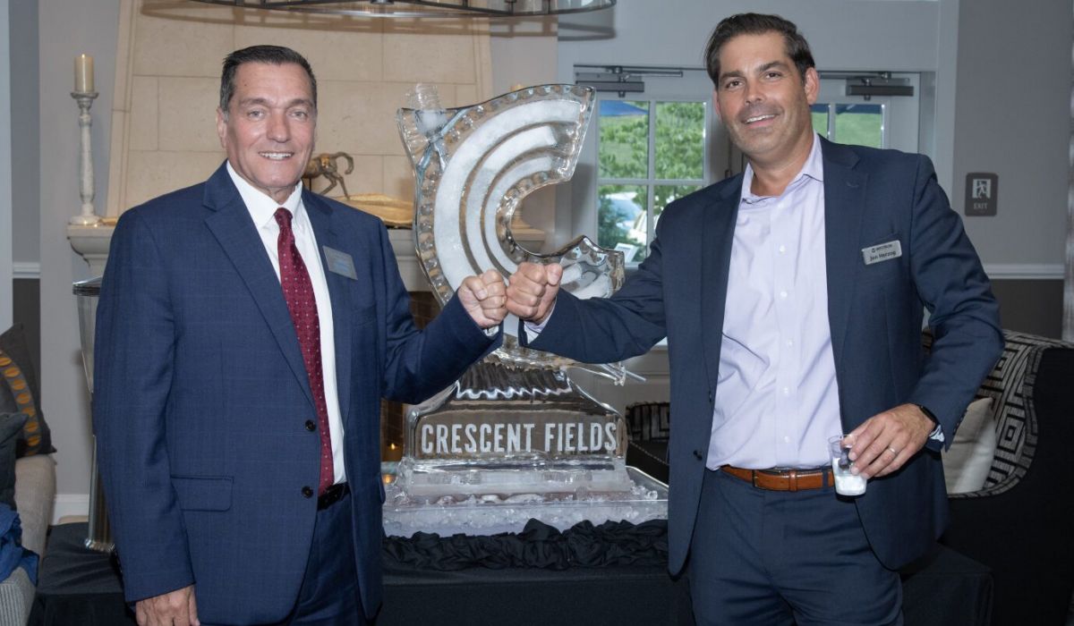 Westrum Corporate Two men in suits smile and fist bump in front of an ice sculpture that reads "Crescent Fields.
