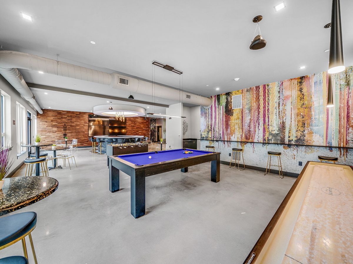 Westrum Corporate Modern West Chester game room with pool table, shuffleboard, Luxor bar seating, vibrant wall art, and bright natural light.
