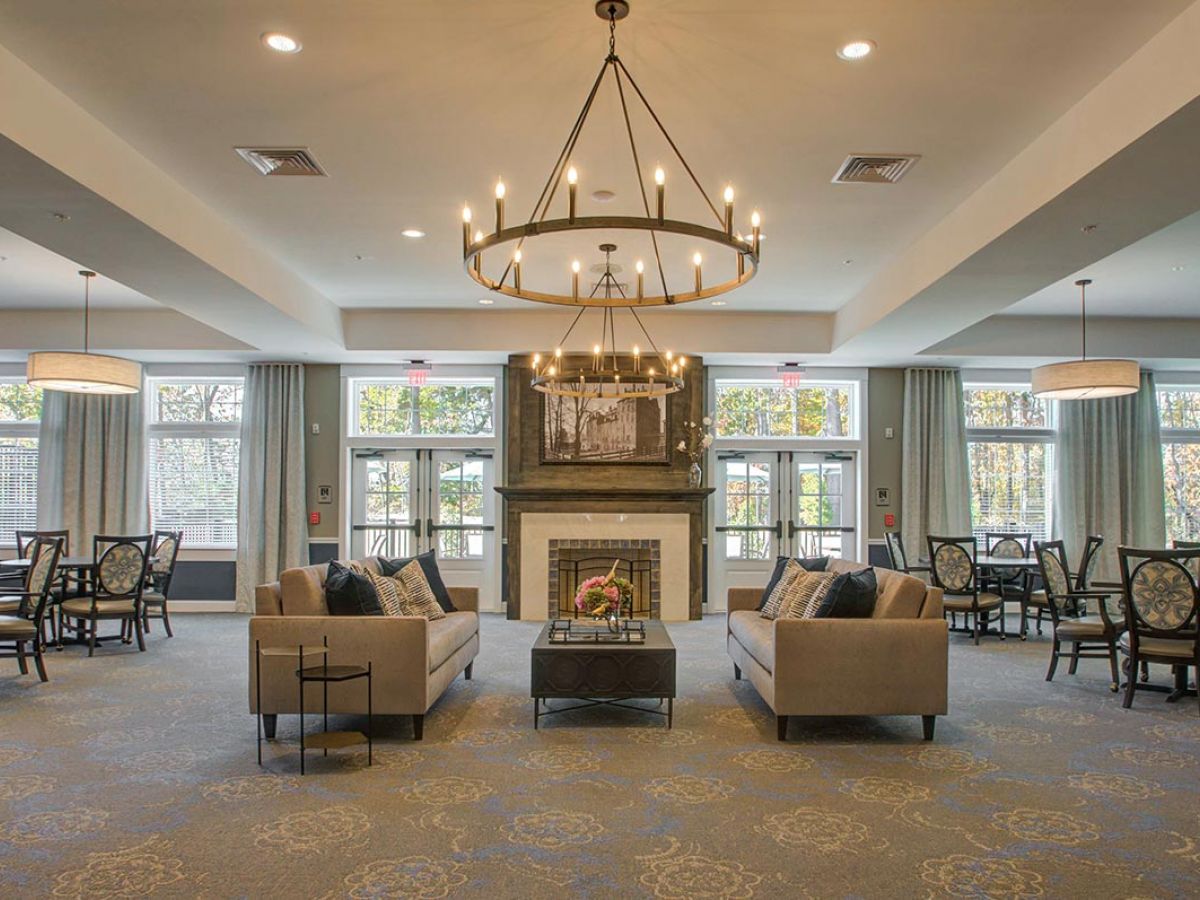 Westrum Corporate Elegant lounge at Mercer Hill, with two sofas facing a fireplace, round chandelier above, and dining tables in the background.