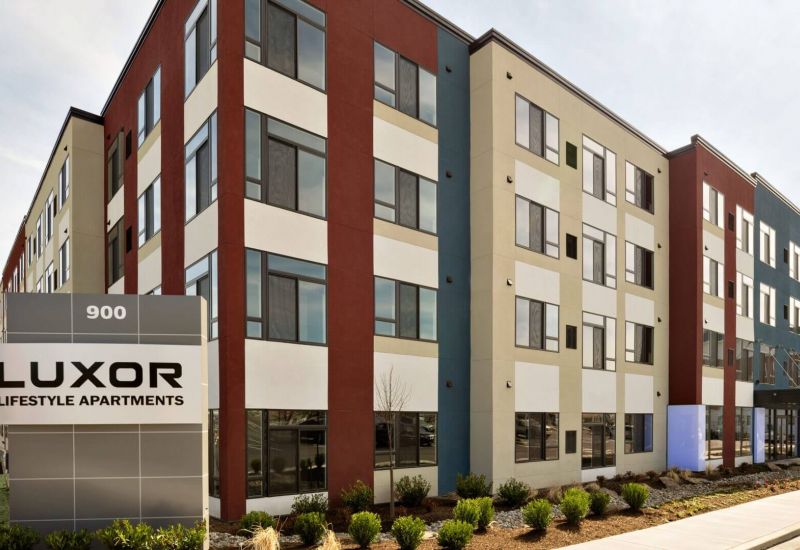 Westrum Corporate Modern four-story building with red, beige, and white accents; Luxor Lifestyle Apartments sign stands prominently in front.
