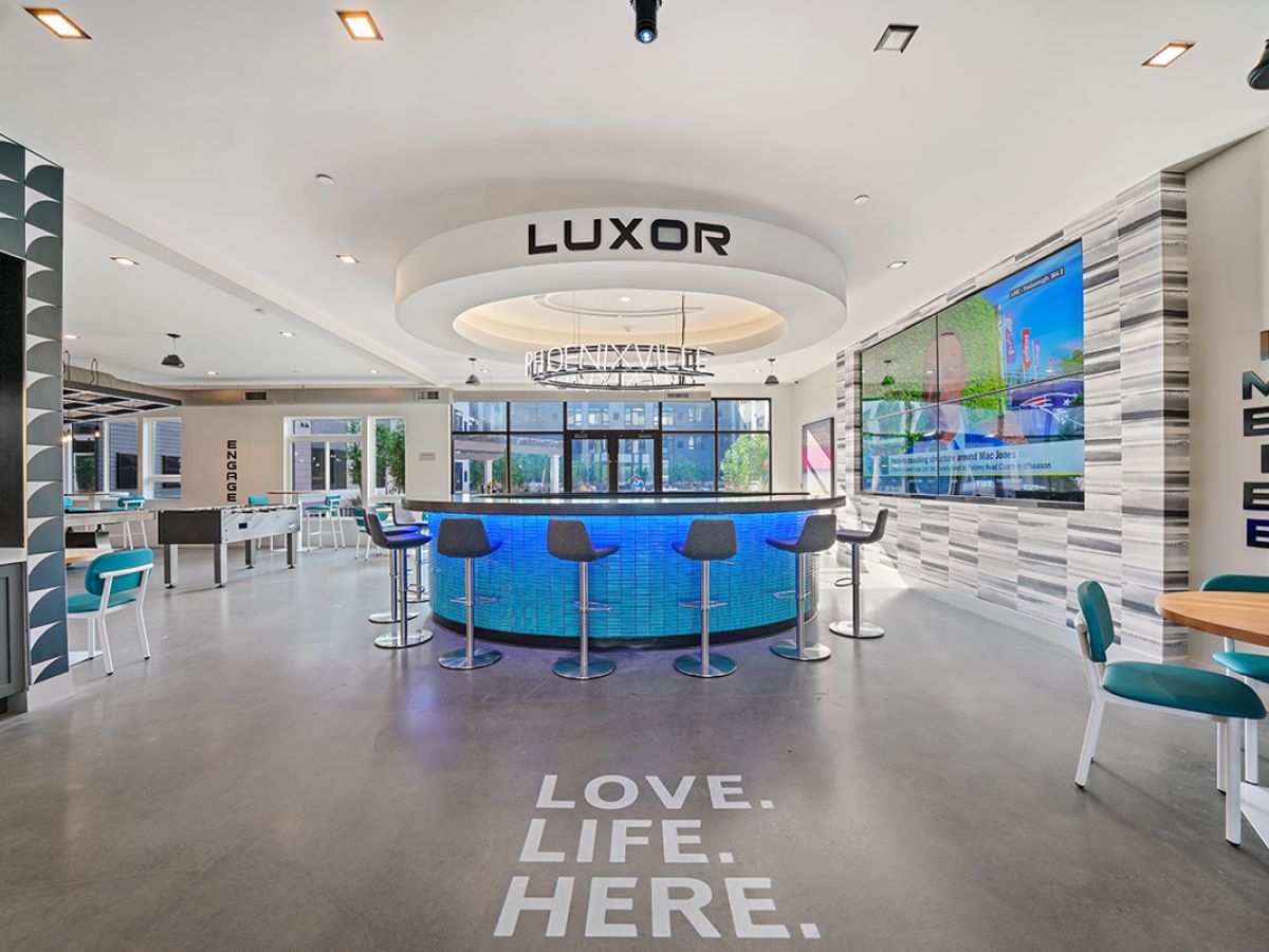 Westrum Corporate Modern lounge in Phoenixville with a circular bar, blue chairs, and “LOVE. LIFE. HERE.” on the floor beneath a Luxor ceiling sign.