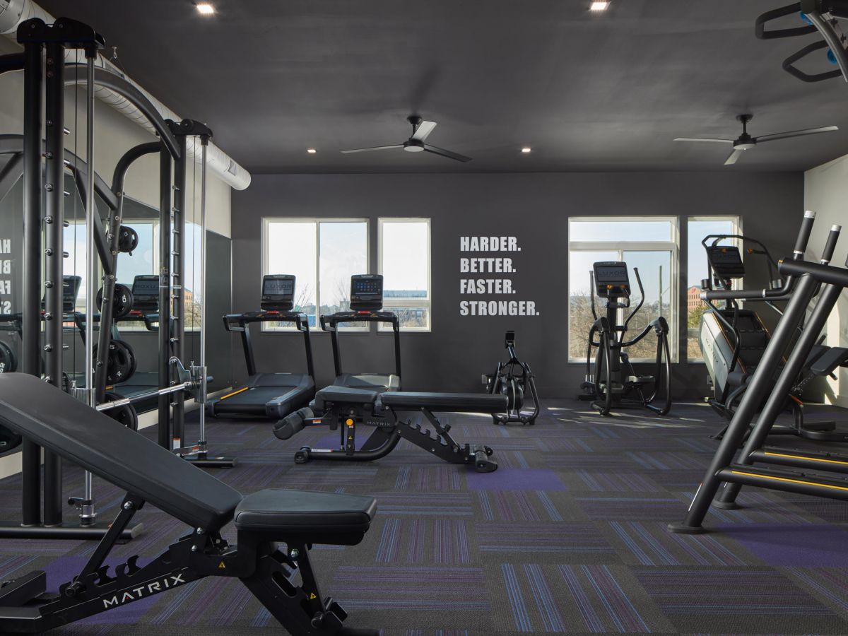 Westrum Corporate Luxor Wilmington features a modern gym with cardio and weight machines, benches, and a "HARDER. BETTER. FASTER. STRONGER." sign.