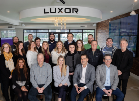 Westrum Corporate A group of 20 people pose together indoors under a LUXOR sign, smiling at the camera.