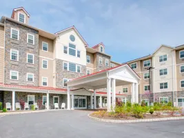 Westrum Corporate Four-story senior living facility with stone and beige siding, white trim, and a covered entrance, set under a blue sky.