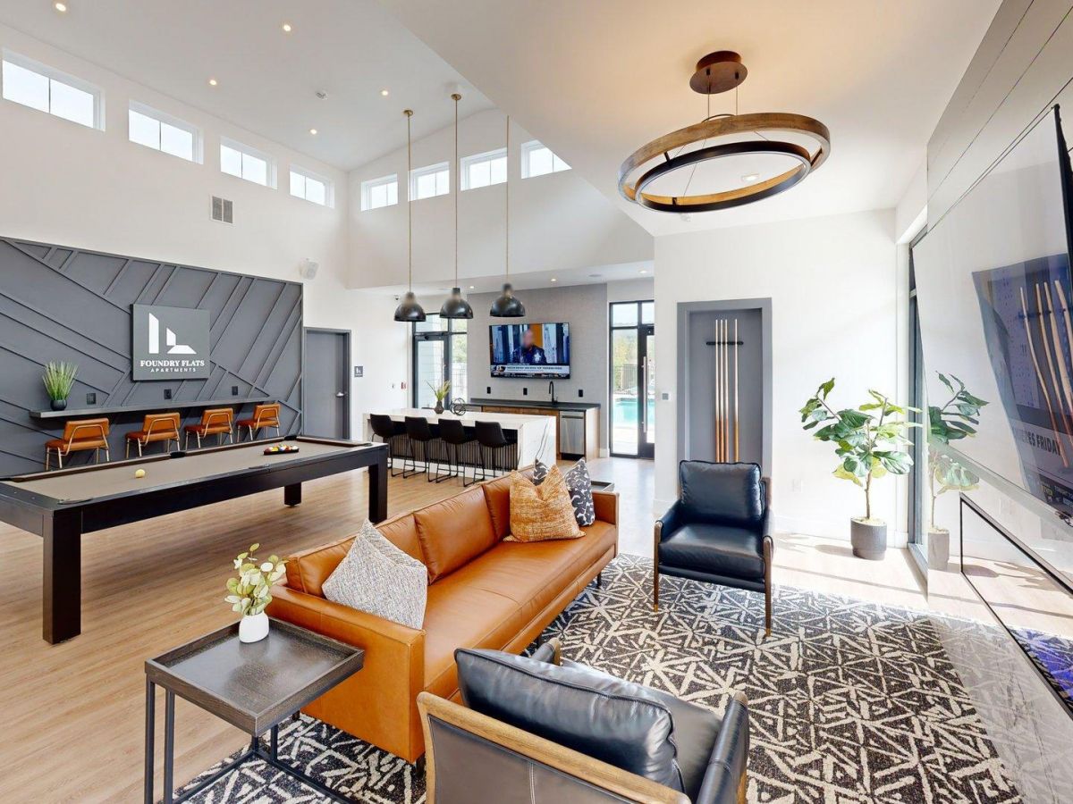 Westrum Corporate Modern lounge at Foundry Flats with a pool table, brown sofa, bar seating, large TV, plants, and high windows letting in natural light.