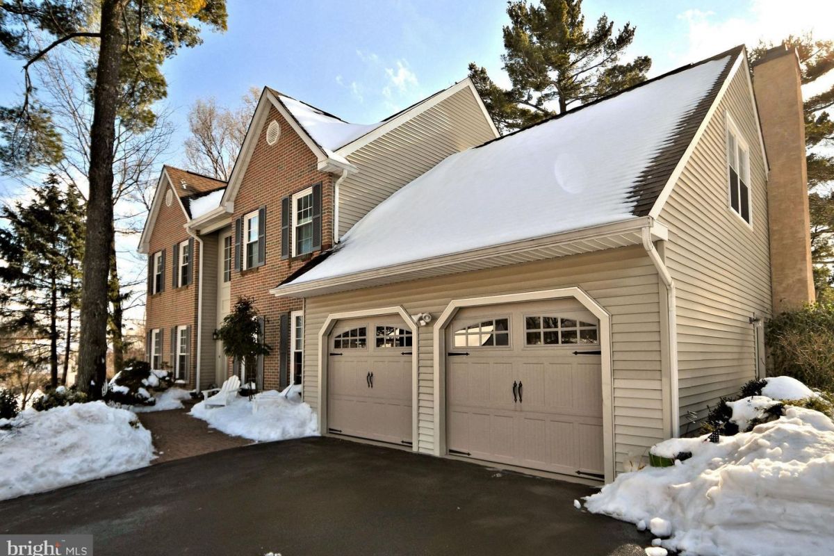 Westrum Corporate Charming two-story Montgomery Township home with brick and siding, snowy roof, double garage, and a driveway dusted in snow.