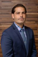 Westrum Corporate Man in a blue suit, plaid shirt, and tie stands in front of a wooden wall, looking directly at the camera.