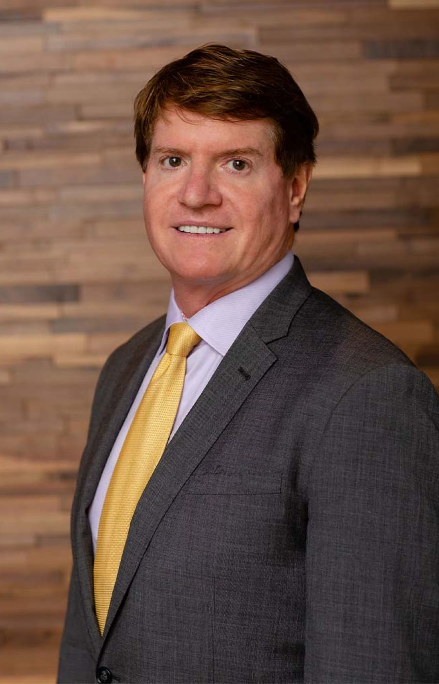 Westrum Corporate John Westrum, in a gray suit and yellow tie, smiles while standing before a wooden background.