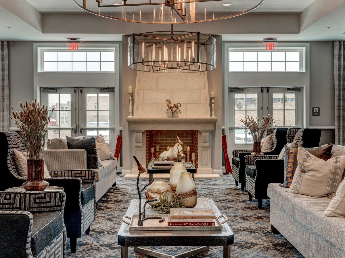 Westrum Corporate Elegant living room with sofas, armchairs, a fireplace, chandelier, coffee table, and large windows letting in natural light.