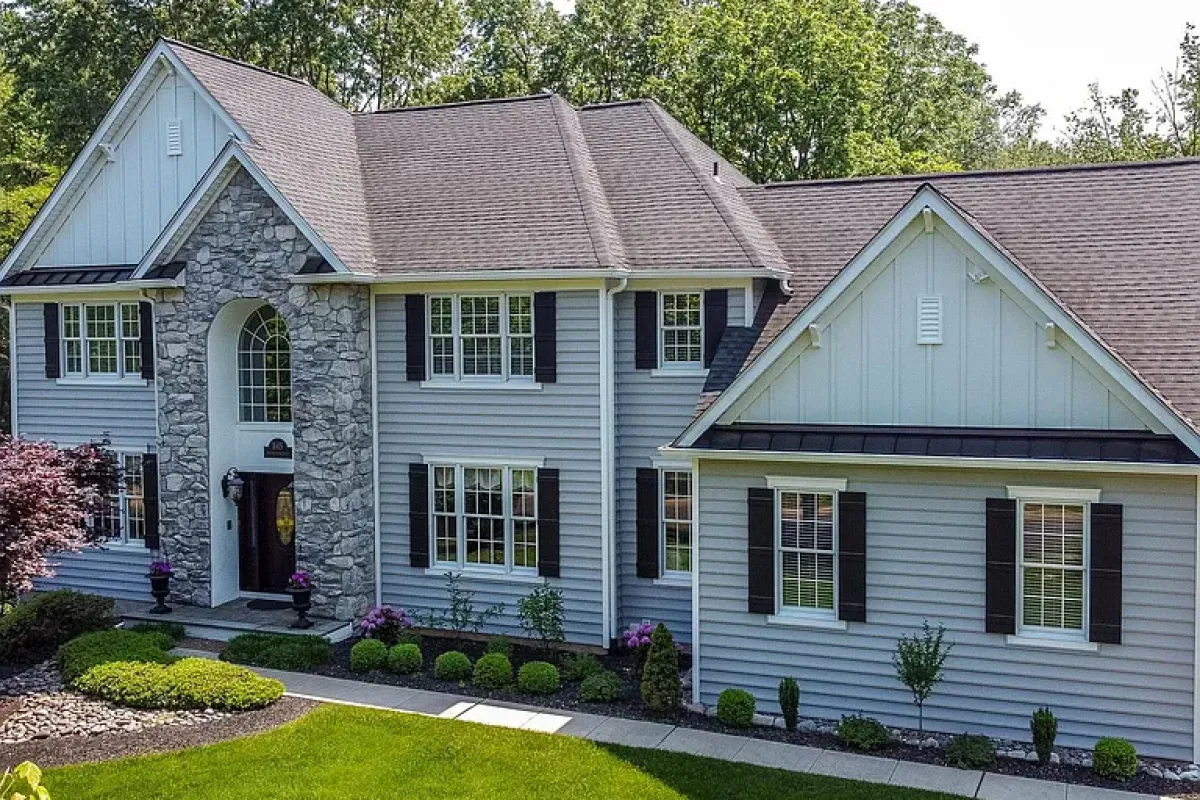 Westrum Corporate Two-story gray house with stone accent in Lower Gwynedd Township, black shutters, manicured lawn, and shrubs surrounded by trees.