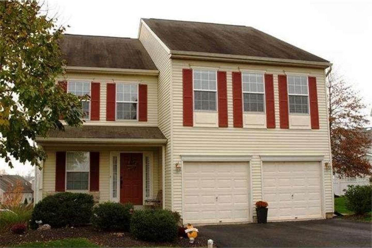 Westrum Corporate Charming two-story beige home in Perkiomen Greene with red shutters, double garage, red door, and bushes lining the front yard.