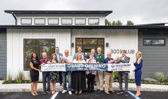 Westrum Corporate Thirteen people stand in front of a building holding a "Grand Opening" banner with the date May 6th, 2026, and smiling at the camera.