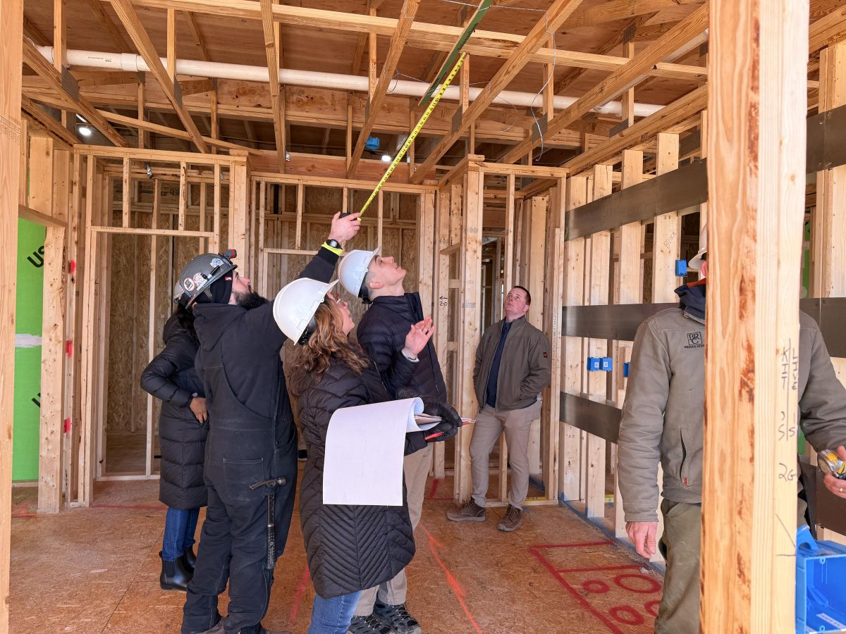 Westrum Corporate Group of people in hard hats inspecting wooden framing inside a building under construction; one measures the ceiling.