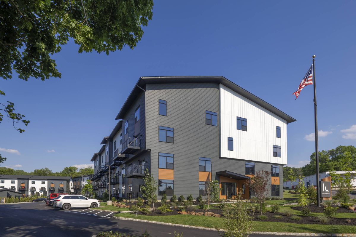Westrum Corporate Foundry Flats is a modern three-story apartment building with cars parked outside, landscaped grounds, and an American flag on a sunny day.
