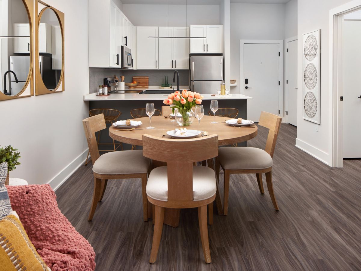 Westrum Corporate Modern kitchen and dining area at Luxor Wilmington with round wooden table, set tableware, white cabinets, and stainless steel appliances.