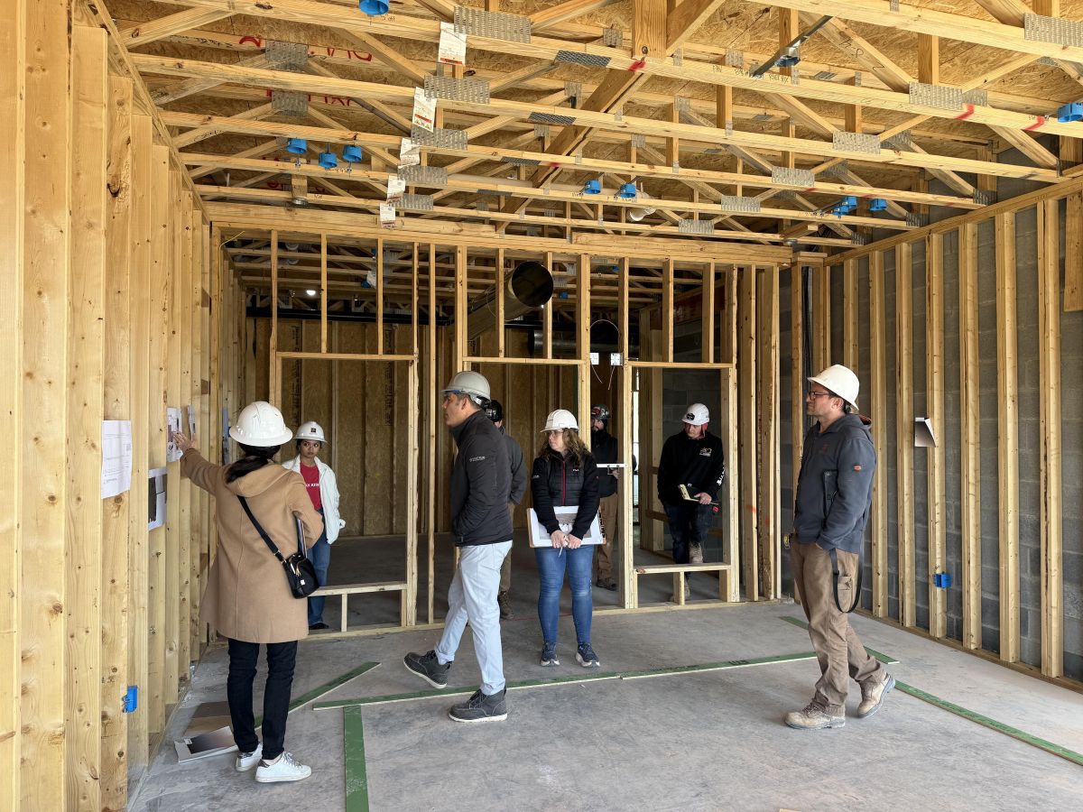 Westrum Corporate Six people wearing hard hats stand inside a wooden building under construction, looking at plans on the wall.
