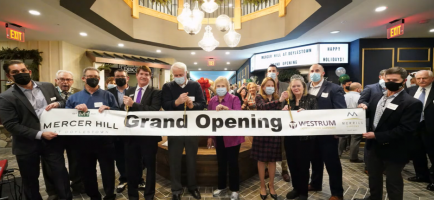 Westrum Corporate A group of people in masks hold a "Grand Opening" banner inside a decorated building lobby, celebrating an event.