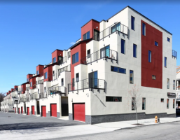 Westrum Corporate Row of modern townhouses with red and white exteriors, balconies, and garage doors under a clear blue sky.