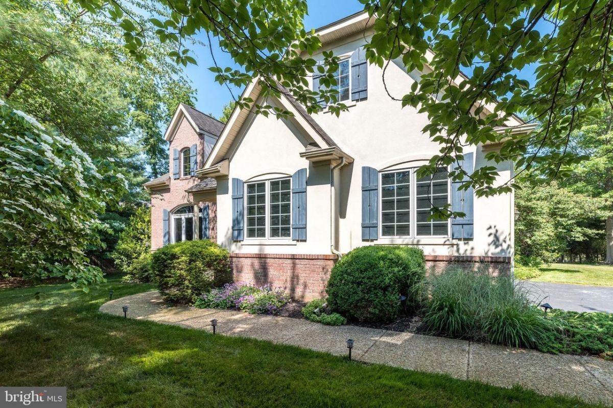 Westrum Corporate Gentry Manor: Two-story house with brick and stucco, large windows, shutters, garden, sidewalk, and trees basking in the sun.