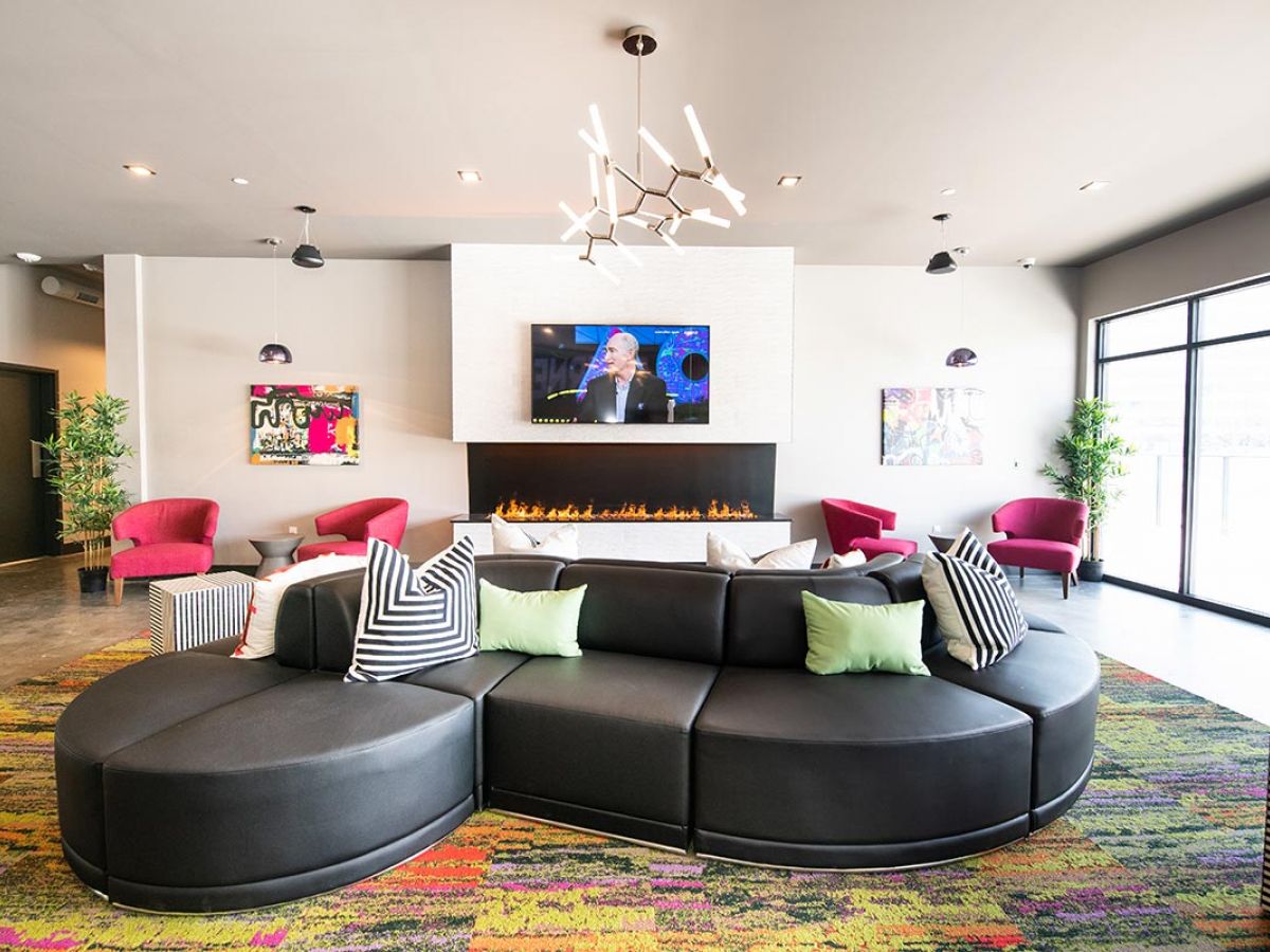 Westrum Corporate Modern lounge at Luxor Bala Cynwyd with a curved black sofa, colorful chairs, wall art, fireplace, and TV in a bright, open space.
