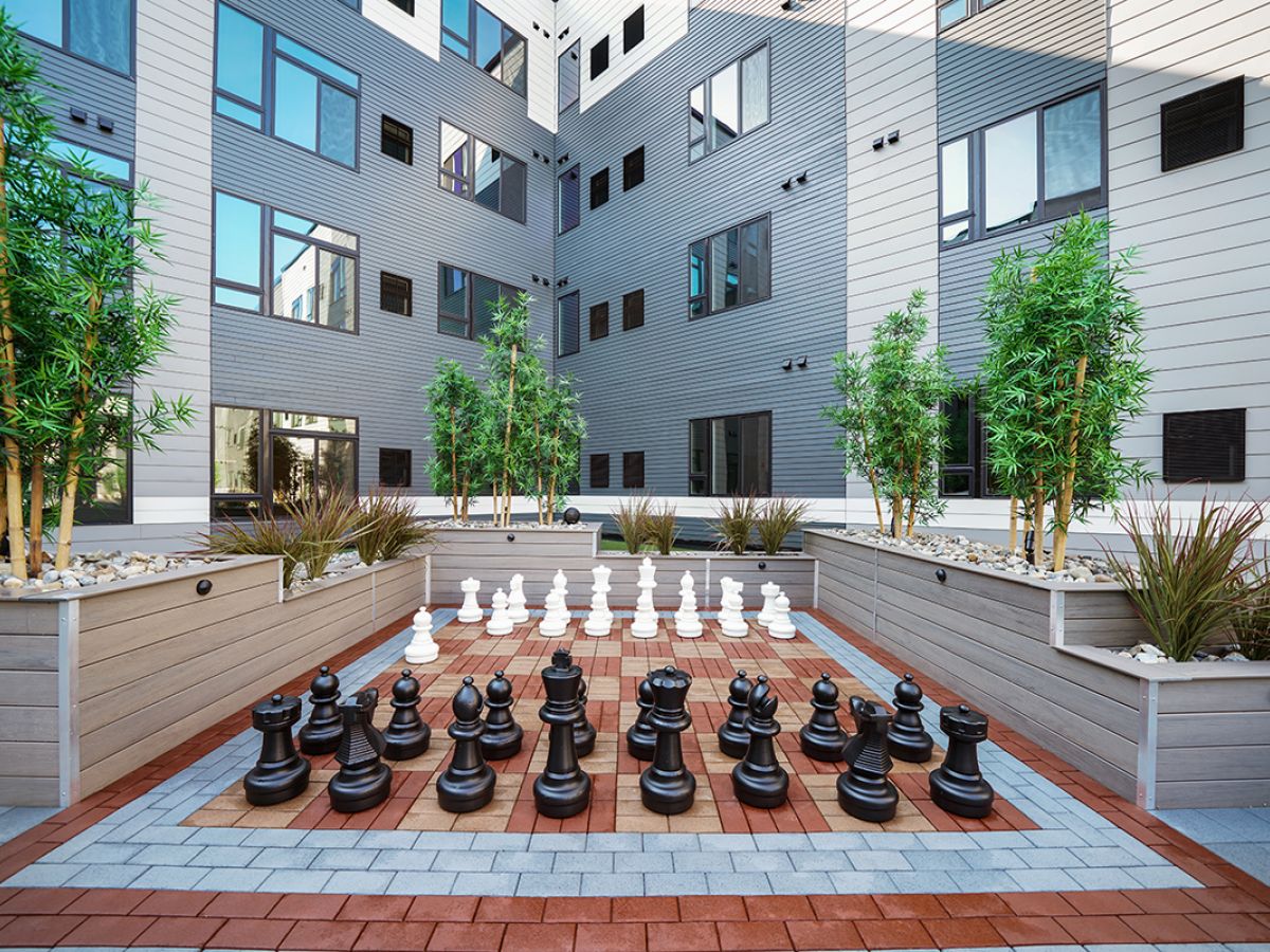 Westrum Corporate Large outdoor chessboard with oversized pieces, surrounded by plants and modern Luxor Phoenixville apartment buildings.