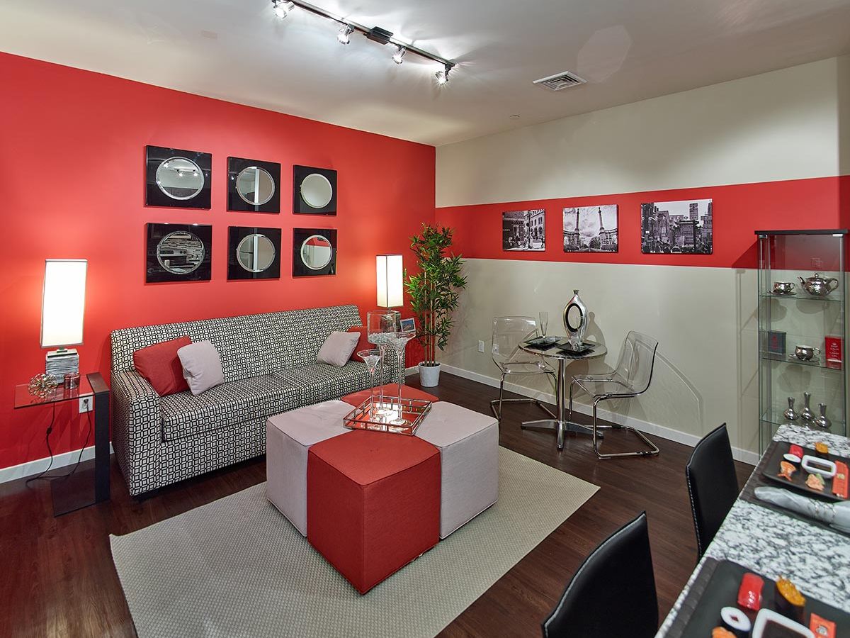 Westrum Corporate Modern living room at Flats at 31 Brewerytown with red accent wall, geometric sofa, glass table, and cityscape art.