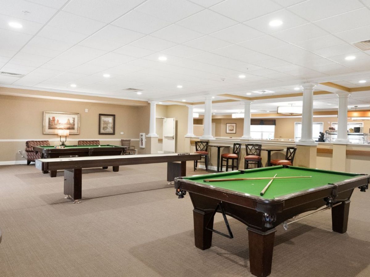 Westrum Corporate Spacious game room at Arbour Square in Harleysville, featuring two billiard tables, barstools, and framed art on tan walls.
