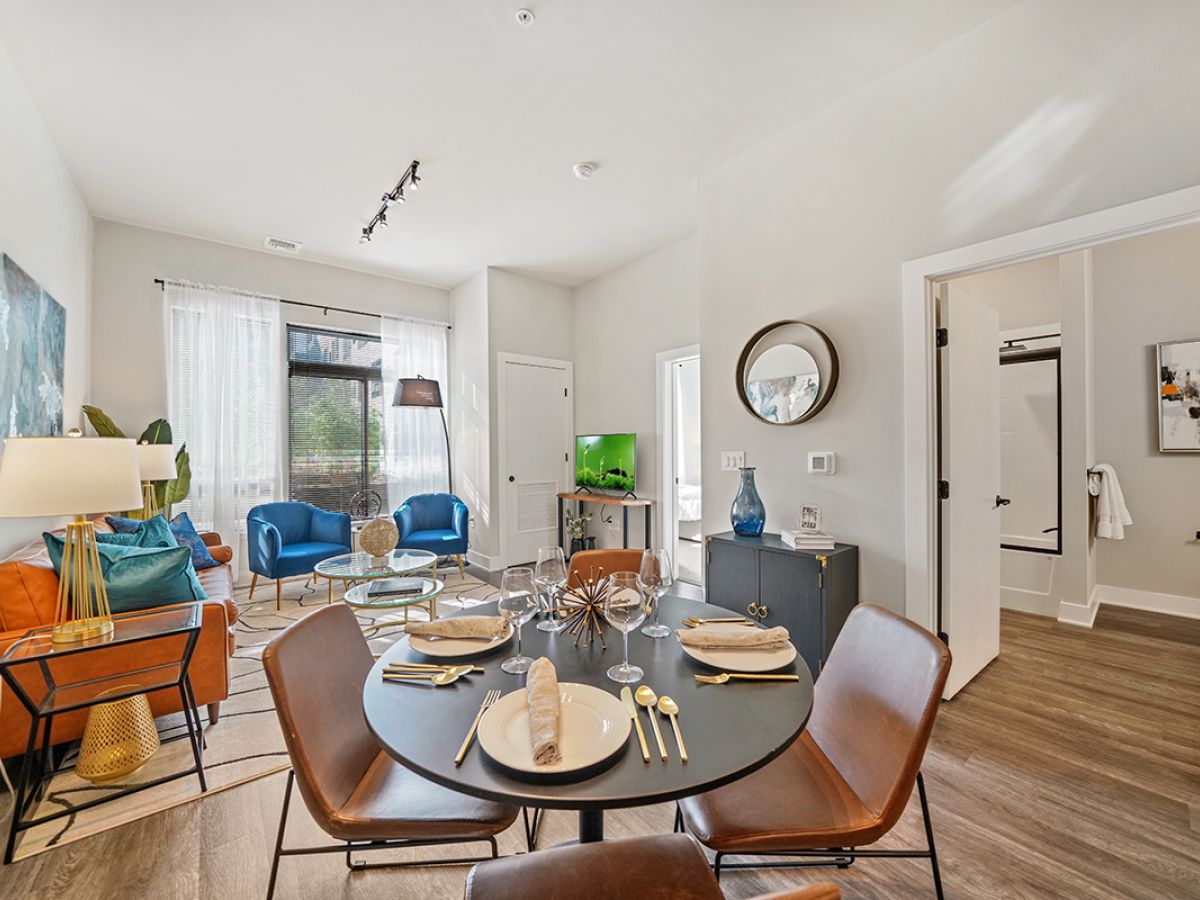 Westrum Corporate Modern Luxor Phoenixville apartment with dining table, cozy living area, colorful chairs, TV, and bathroom visible; bright natural light.