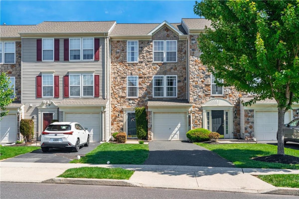 Westrum Corporate Three-story Greenbriar townhouse with stone and siding, red shutters, white car in driveway, green lawn, and a tree at right.