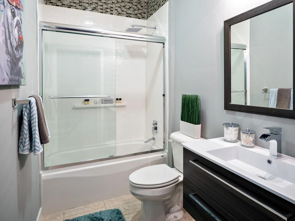 Westrum Corporate Modern bathroom in 1200 Washington with glass shower, white sink, dog wall art, and a mirror above a dark vanity.