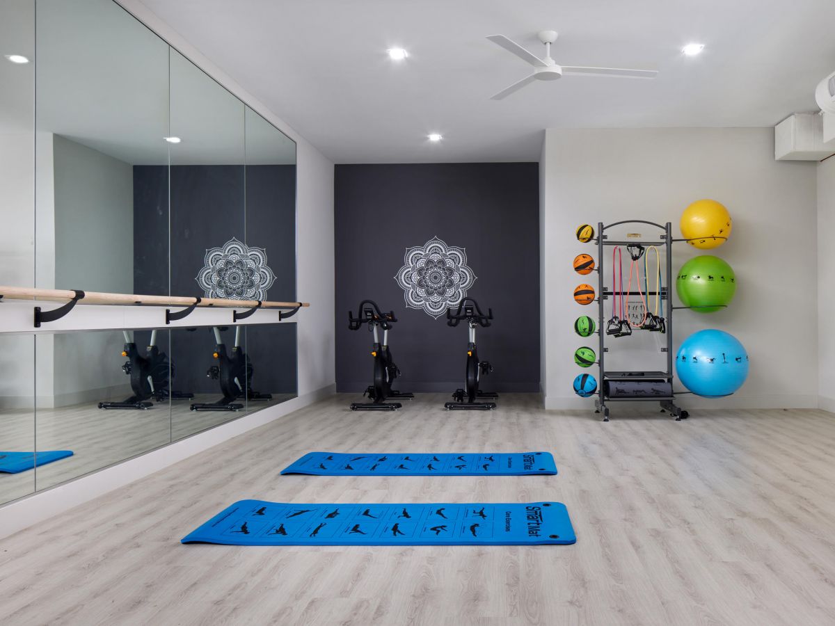 Westrum Corporate Modern Luxor Wilmington gym room with bikes, blue mats, wall mirrors, and medicine balls on light wood flooring.