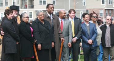 Westrum Corporate A group of people in business and casual attire pose for a photo outdoors in front of apartment buildings.
